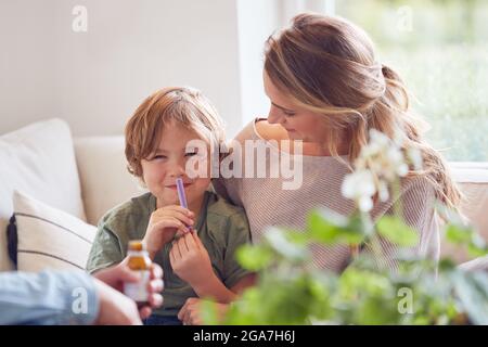 Parents Giving Son Medicine With Syringe Sitting On Sofa At Home Stock Photo