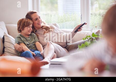 Mother Relaxing With Children On Sofa At Home Watching TV Together Stock Photo