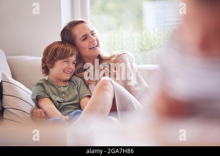 Mother Relaxing With Children On Sofa At Home Watching TV Together Stock Photo