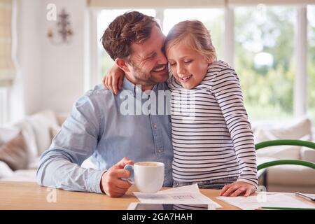 Loving Daughter At Home With Father Sitting At Table With Paperwork Stock Photo