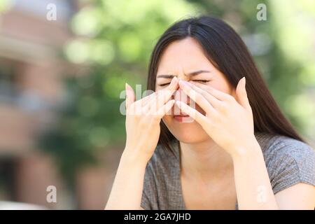Stressed asian woman scratching itchy eyes in the street Stock Photo