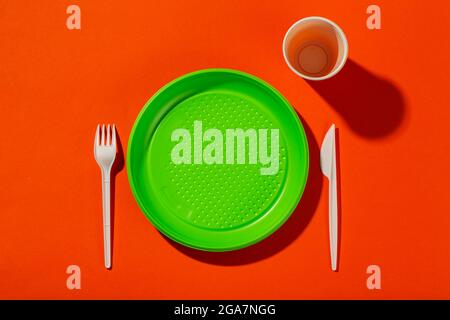Plastic set of disposable tableware consisting of a plate, knife, cup and fork on an orange background. Environmental concept. Ban single use plastic. Stock Photo