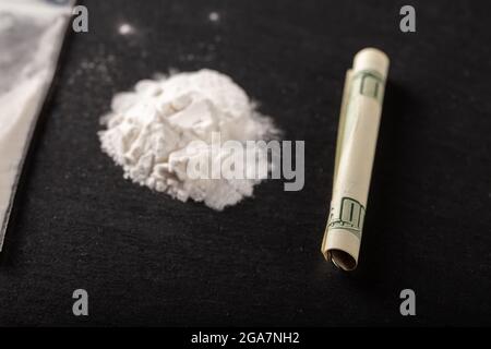 Cocaine in a plastic package on a black background, close-up. A rolled up dollar bill for drug use. Prohibited drugs. Stock Photo