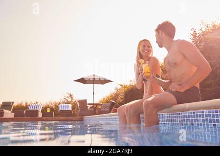 Loving Couple On Summer Vacation Sitting On Edge Of Swimming Pool With Cold Drinks Stock Photo