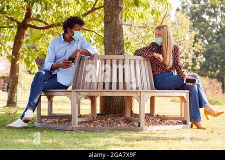 Socially Distanced Couple Wearing Masks Meeting In Outdoor Park During Health Pandemic Stock Photo