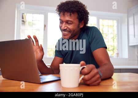 Mature Man At Home In Kitchen Waving As He Makes Video Call On Laptop Computer Stock Photo