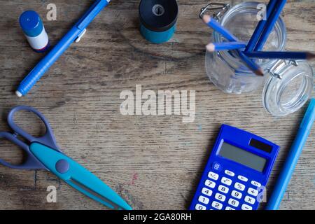 blue coloured school supplies on vintage wood desk top, including scissors, calculator, pencils, glue eraser and pencil sharpener, with copy space Stock Photo