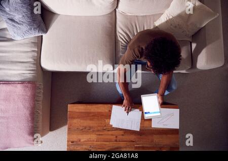 Overhead Shot Of Man Working From Home Sitting On Sofa Reviewing Documents Using Digital Tablet Stock Photo