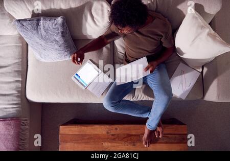 Overhead Shot Of Man Working From Home Sitting On Sofa Reviewing Documents Using Digital Tablet Stock Photo