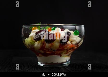 Salad from grapes apples pears kiwi oranges with mascarpone chease and cream. Healthy fresh fruit summer salad in glass bowl on black wooden backgroun Stock Photo