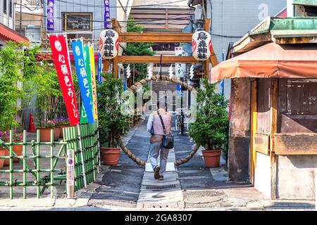 Tokyo, Japan - 21st June 2016: Men walk through a side street in downtown Tokyo. Colourful lanterns and flags hang outside the local bars and restaura Stock Photo