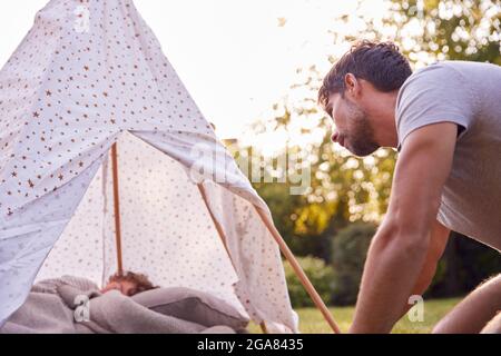Loving Father Looking In On Son Sleeping Inside Tent Or Tepee Pitched In Garden Stock Photo
