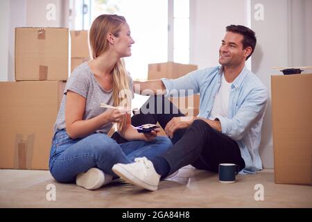 Couple Celebrating With Takeaway Sushi Meal Sitting On Floor Of New Home On Moving Day Stock Photo