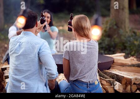 Group Of Friends Camping Sitting By Bonfire In Fire Bowl Celebrating And Drinking Beer Together Stock Photo