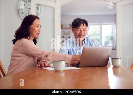 Mature Asian Couple At Home Using Laptop To Organise Household Bills And Finances Stock Photo