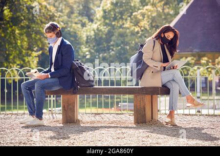 Businessman And Businesswoman Wearing Masks On A Break Reading Book And Watching Digital Tablet Stock Photo