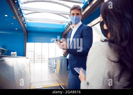 Business Couple Commuting Riding Escalator At Railway Station Wearing PPE Face Masks In Pandemic Stock Photo