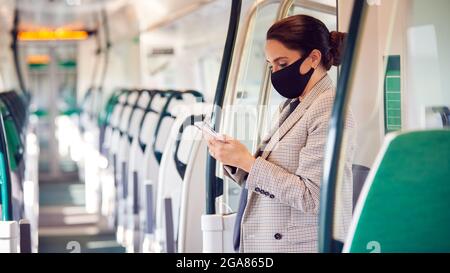Businesswoman Stands In Train Carriage Using Mobile Phone Wearing PPE Face Masks During Pandemic Stock Photo