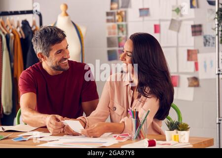 Male And Female Fashion Designers In Studio Working On Sketches And Designs At Desk Stock Photo