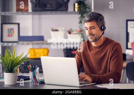 Mature Businessman Wearing Telephone Headset Talking To Caller In Customer Services Department Stock Photo