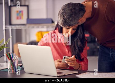 Man In Office Comforting Female Work Colleague Upset By Mobile Phone Message In Office Stock Photo