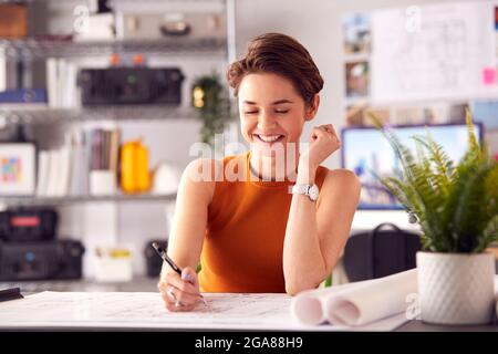 Female Architect In Office Working At Desk Making Notes On Plan Or Blueprint Stock Photo