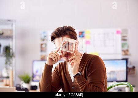 Portrait Of Male Architect In Office Working At Desk Looking Through Wooden Model Of Building Stock Photo