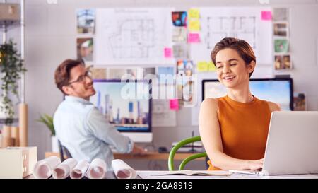 Male And Female Architects In Office Working At Desk On Laptop And Desktop Computers Stock Photo