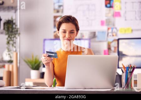 Female Architect In Office Working At Desk Making Online Purchase Using Credit Card On Laptop Stock Photo