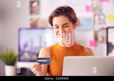 Female Architect In Office Working At Desk Making Online Purchase Using Credit Card On Laptop Stock Photo