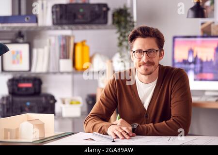 Portrait Of Male Architect In Office Working At Desk With Model Of Building Stock Photo