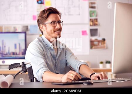 Disabled Female Architect In Wheelchair In Office Working On Desktop Computer Using Graphics Tablet Stock Photo