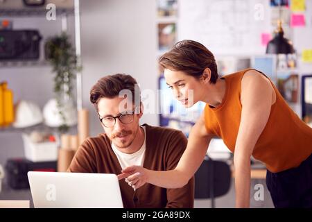 Male And Female Architects In Office Working At Desk On Laptop And Looking At Plans Stock Photo