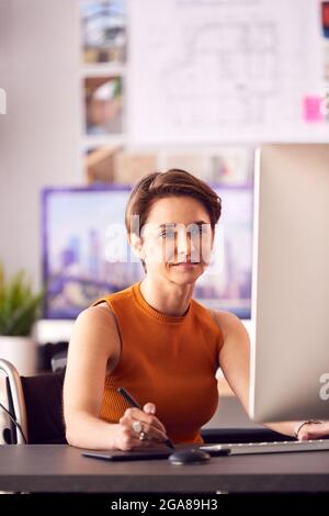 Disabled Female Architect In Wheelchair In Office Working On Desktop Computer Using Graphics Tablet Stock Photo