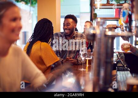 Smiling Young Couple On Date Sitting At Counter Of Busy Bar Stock Photo