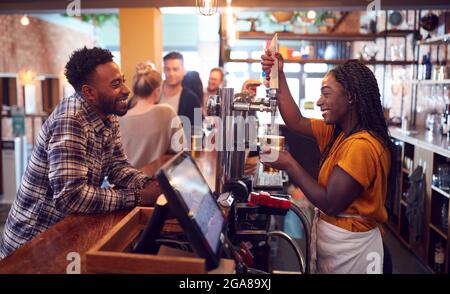 Smiling Female Bartender Behind Counter Serving Female Customer With Beer Stock Photo