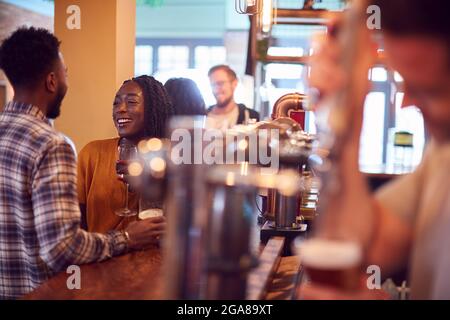 Smiling Young Couple On Date Sitting At Counter Of Busy Bar Stock Photo
