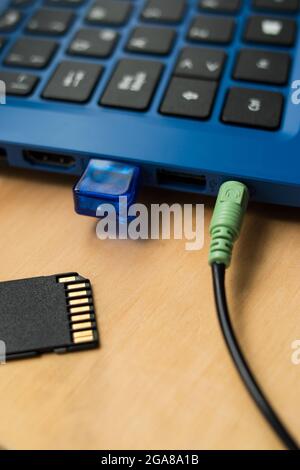 Earphones cables connected to a blue modern laptop, USB memory  and SD memory on a wooden table Stock Photo