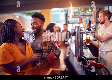 Smiling Young Couple On Date Sitting At Counter Of Busy Bar Stock Photo
