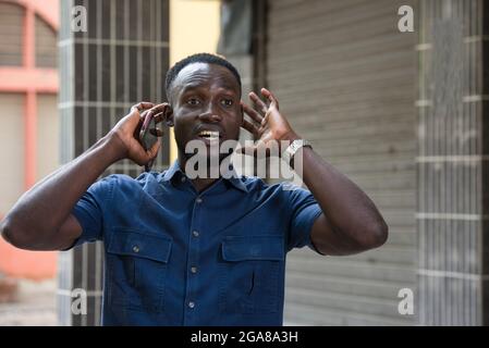 surprised man holds a cell phone in hand holds his ears while listening to a sound outside Stock Photo