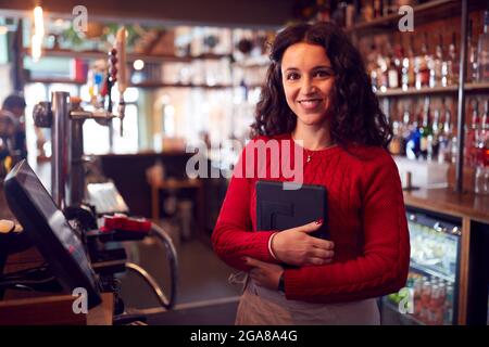 Portrait Of Smiling Female Bar Owner With Digital Tablet Standing Behind Counter Stock Photo