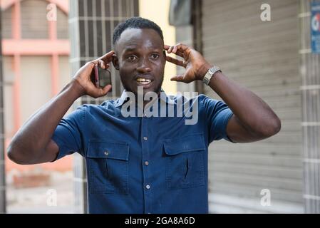 surprised man holds a cell phone in hand holds his ears while listening to a sound outside Stock Photo