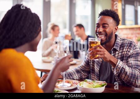 Smiling Young Couple On Date Making Toast Before Enjoying Pizza In Restaurant Together Stock Photo