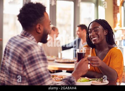 Smiling Young Couple On Date Making Toast Before Enjoying Pizza In Restaurant Together Stock Photo