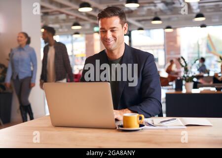 Businessman Sitting At Desk Working On Laptop In Modern Open Plan Office Stock Photo