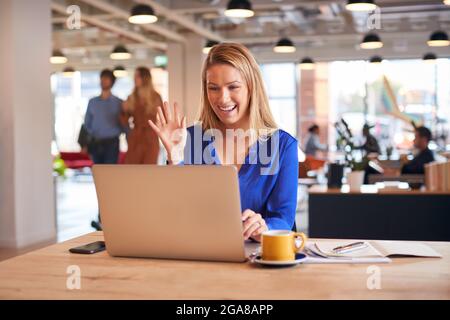 Young Businesswoman Sitting At Desk On Video Call In Modern Open Plan Office Stock Photo