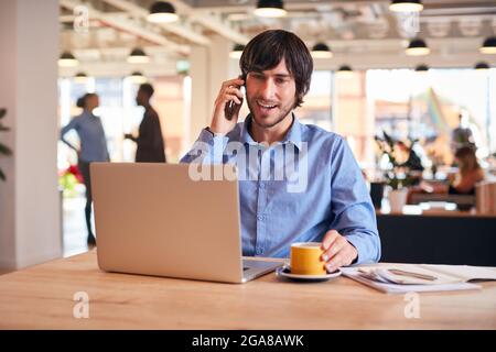 Businessman Sitting At Desk On Phone Call In Modern Open Plan Office Stock Photo