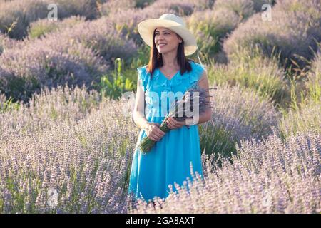 Beautiful young woman in wicker hat and blue dress posing in a lavender field Stock Photo