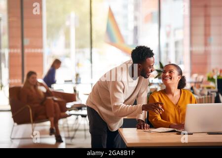 Businessman And Businesswoman Having Informal Meeting By Desk In Modern Open Plan Office Stock Photo