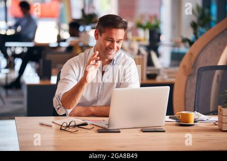 Businessman Sitting At Desk On Video Call In Modern Open Plan Office Stock Photo